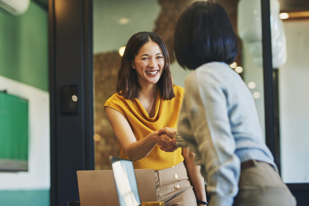 Cheerful businesswomen shaking hands in meeting room